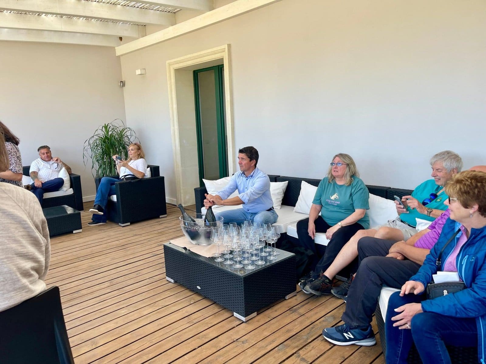 Group of guests on a wooden patio at Cantele Winery, with champagne in an ice bucket and many glasses.